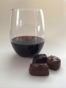 image of wine and chocolate, wine glass next to chocolate, red wine with three chocolates, stemless wine glass with red wine, stemless wine glass